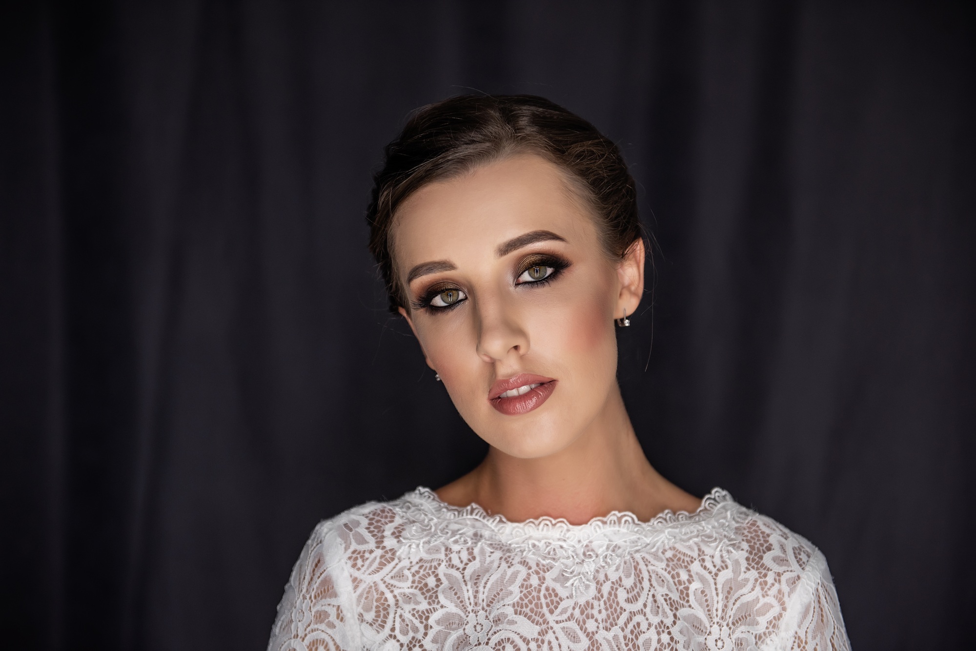Close-up portrait of fashion bride in white vintage openwork dress on black fabric background.