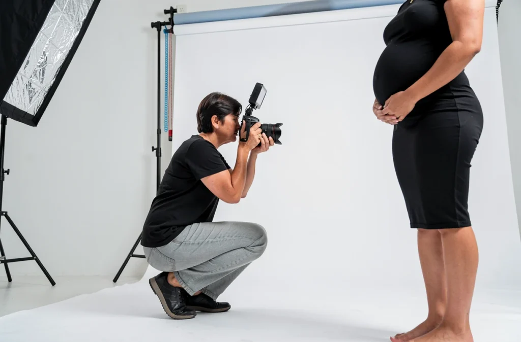 Photographe professionnelle ajustant son cadrage lors d'une séance photo grossesse en studio avec une femme enceinte